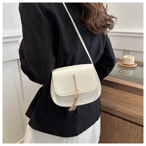 Detail of cream white crossbody bag with gold tassel hardware on a black blazer outfit
