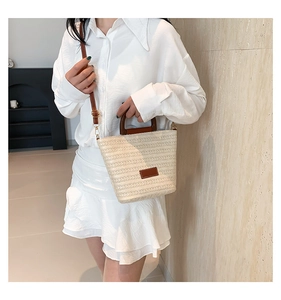 Détail de la texture en fibre tissée et garniture en cuir brun sur un sac seau beige