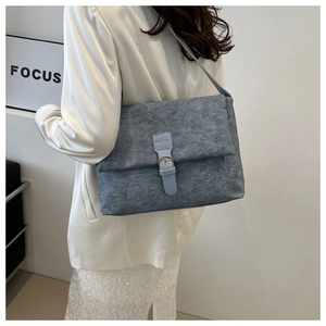 Détail du sac bandoulière bleu clair à texture froissée et boucle sur blazer blanc