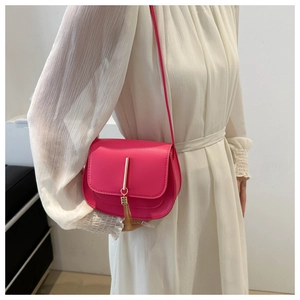 Detail of rose red saddle bag with gold metal trim and tassel on white dress