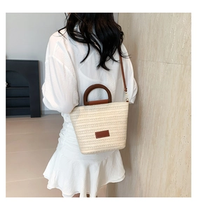 Détail d'un sac cabas en paille tissée avec poignée en bois brun et bandoulière fine