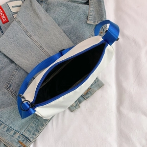 Top view of white and blue canvas crossbody bag with blue nylon strap on denim jacket