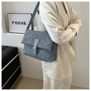 Détail d'un sac à bandoulière gris mat avec lanière bleue sur un mannequin en tailleur