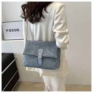 Détail du sac bandoulière gris-bleu en cuir dépoli avec boucle sur un blazer blanc
