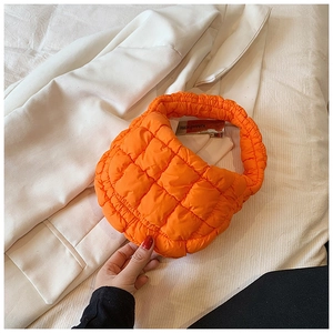 Detailed close-up of quilted orange cloud handbag with Kimhekim label on soft white jacket