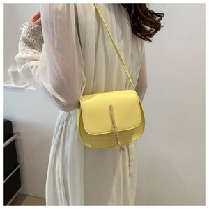 Close-up of yellow crossbody bag with gold metal fringe tassel worn with white dress