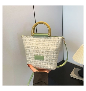 Détail d'un sac en paille tressée avec poignées en cuir vert et bandoulière réglable