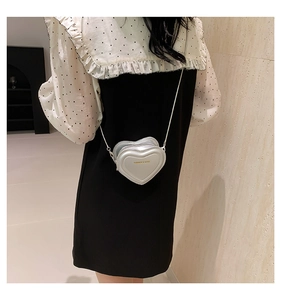 Detail of silver heart-shaped mini crossbody bag with gold text and chain strap on model