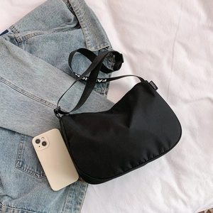 Detail of black canvas crescent bag with FASHION strap text on casual denim jacket