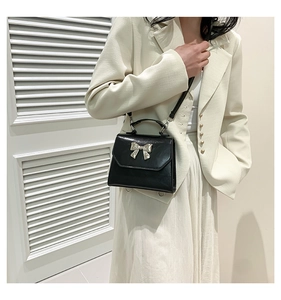Detail view of black glossy leather handbag with silver metal bow and adjustable strap