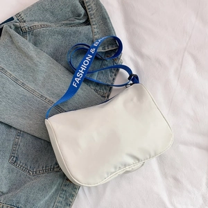 Detail of white canvas crossbody bag with blue fashion strap and denim jacket
