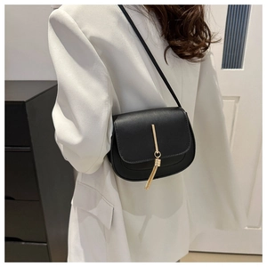 Detail of minimalist black saddle bag with golden metal clasp and tassel pendant decoration