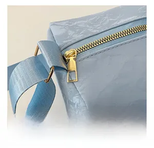 Close-up of golden zipper hardware and pleated leather texture on a light blue shoulder bag