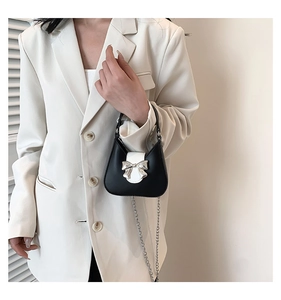 Detail of a contrast saddle bag featuring a silver bow buckle and elegant metal chain strap