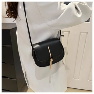Detail of black leather crossbody bag featuring gold metal bar and elegant tassel fringe