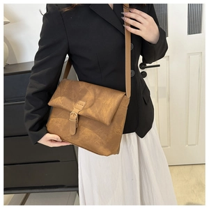 Détail d'un sac bandoulière vintage marron avec boucle en métal porté sur une veste noire