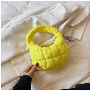 Detail of a bright yellow quilted nylon puff handbag placed on a white blazer