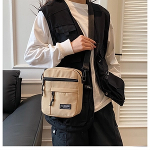 Khaki canvas crossbody bag with front zipper and fashion label shown on a model