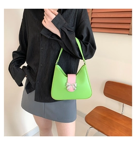 Close-up of stylish green saddle bag featuring a pink strap and silver metal bow decoration