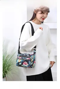 Detail of floral nylon crossbody bag with adjustable strap worn by model on white sweater