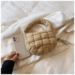 Detailed macro view of beige quilted bubble tote bag with smartphone for size reference