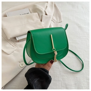 Close-up of bright green leather saddle bag featuring gold metal bar and tassel detail