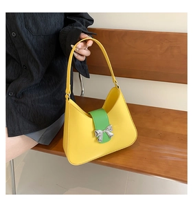 Close-up of yellow and green contrast saddle bag with silver bow buckle on wooden bench