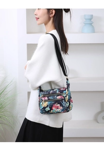 Detail showing multi-zipper floral nylon crossbody bag with adjustable black strap on model