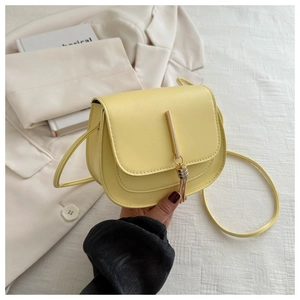 Detail of yellow leather saddle bag showing metal bar tassel and flip cover closure
