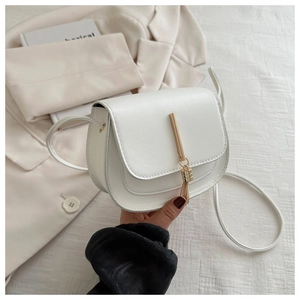 Detail of white saddle bag featuring gold tassel hardware and smooth PU leather finish