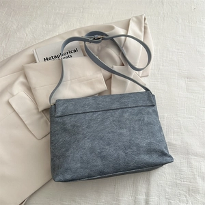 Sac fourre-tout gris-bleu en cuir dépoli sur un blazer ivoire dans un décor apaisant