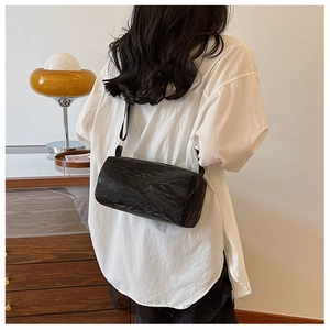 Detail of a black cylinder shoulder bag with a unique pleated texture on a model