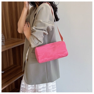 Pink cylinder shoulder bag with unique paper-fold texture shown on female model in grey suit