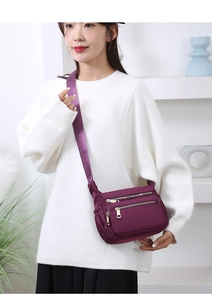 Detail view of purple nylon crossbody bag with three silver zippers and woven strap