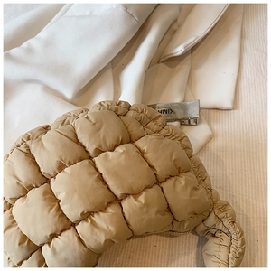 Detail of beige quilted puffer baguette bag showing soft square padding and metal zipper