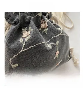 Détail de la broderie de rose sur le sac seau en maille grise avec cordon de serrage