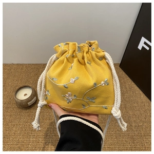 Détail d'un petit sac en toile jaune avec broderies florales et fermeture à cordon en coton