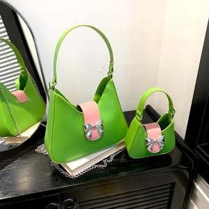 Fashionable green saddle shoulder bag with pink strap and silver metal bow detail
