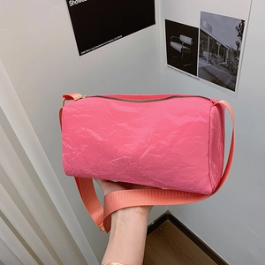 Pink cylinder shoulder bag with textured surface and wide strap held by a model