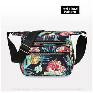Macro detail of red floral nylon crossbody bag featuring multiple zipper pockets and strap