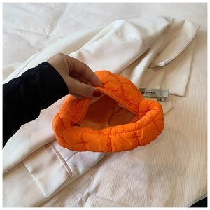 Detail of bright orange quilted puffy clutch showing zip closure and internal storage