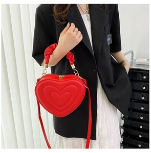 Detail of red heart-shaped pleated handbag with golden hardware and slender strap