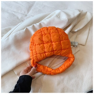 Close-up of vibrant orange quilted puffy cloud handbag with glossy polyester fabric texture