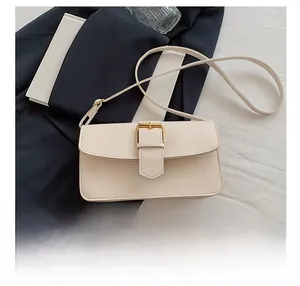 Detail show of a cream rectangular leather shoulder bag with a gold buckle on blue fabric