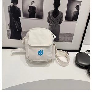 Nahaufnahme einer weißen Canvas-Umhängetasche mit blauem Sticklogo und vorderer Klappentasche