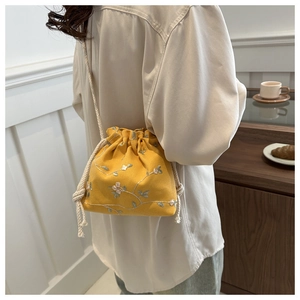 Détail du sac seau jaune à cordon avec broderie florale délicate et bandoulière en corde