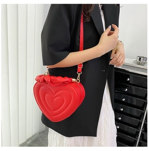 Detail of red heart-shaped crossbody bag featuring quilted layers and ruffle trim