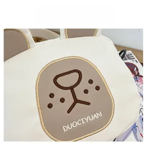 Close-up of cream white canvas bag showing bear embroidery and DUOCIYUAN text detail