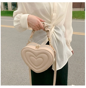 Detail of a beige heart-shaped crossbody bag with quilted layers and ruffled handle