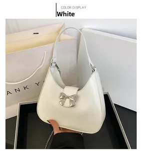 Detailed view of a white hobo shoulder bag with a silver metal bow and delicate chain